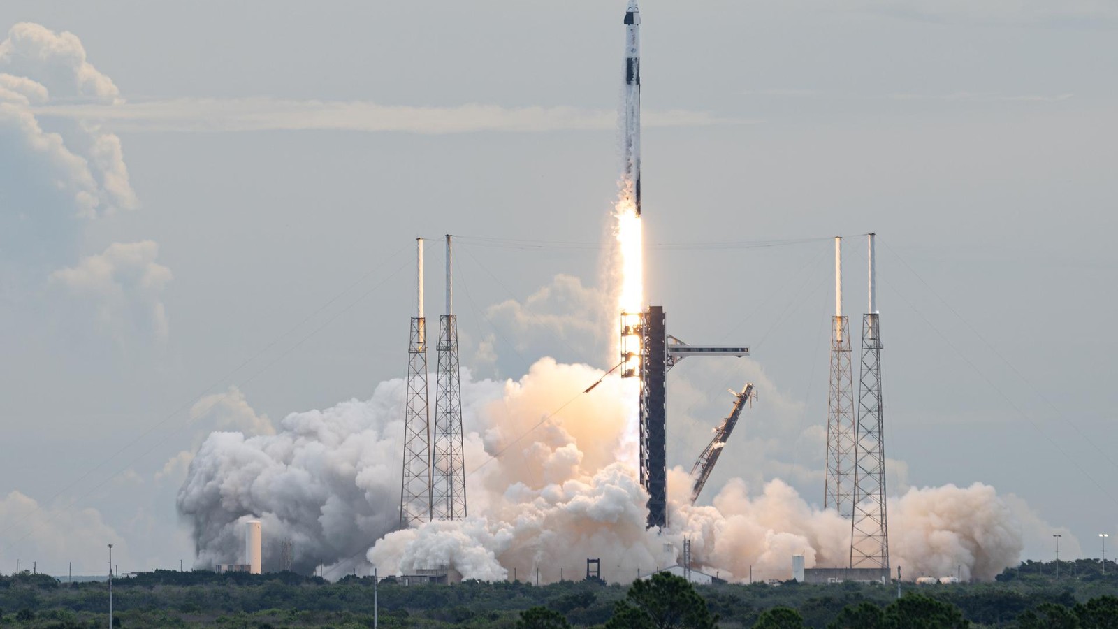 Un cohete Falcon 9 con la cápsula Dragon despega entre una gran columna de humo