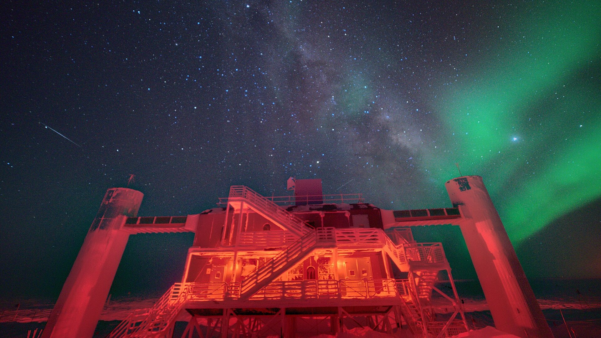 El laboratorio de IceCube en el Polo Sur, iluminado de rojo bajo la Vía Láctea y una aurora austral verde