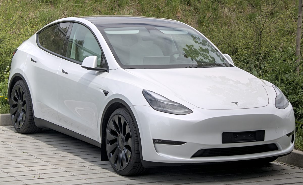 Un Tesla Model Y blanco aparcado sobre una superficie de madera junto a un seto